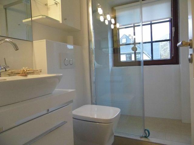 Badezimmer mit Dusche, Waschbecken und Toilette. Fenster mit Holzrahmen.