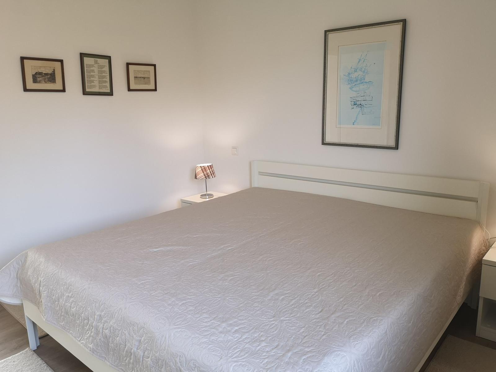 Schlafzimmer mit Bett, Nachttisch und Wandbildern.