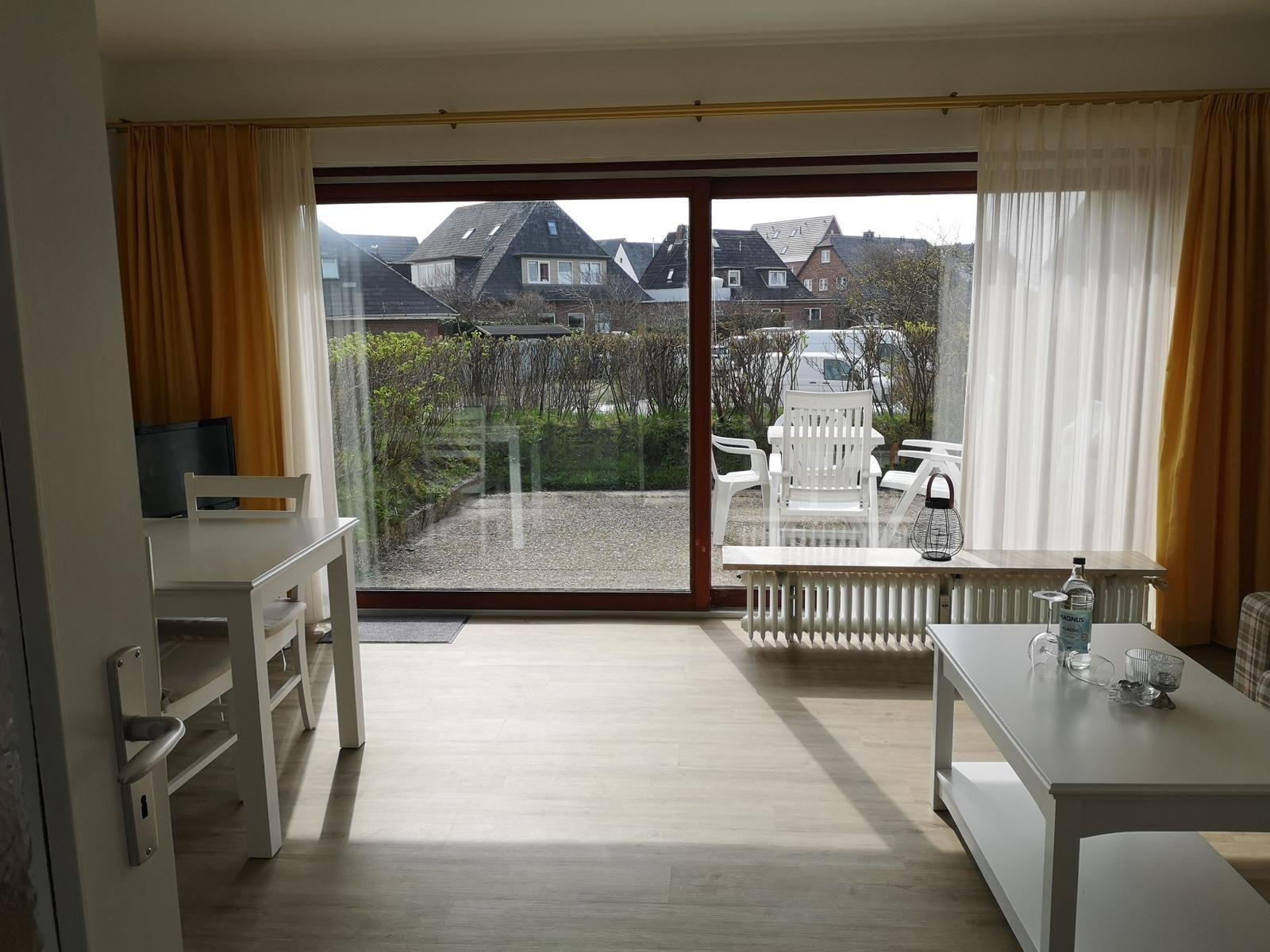 Wohnraum mit Blick auf Terrasse und Garten. Weiße Möbel und große Fenster.