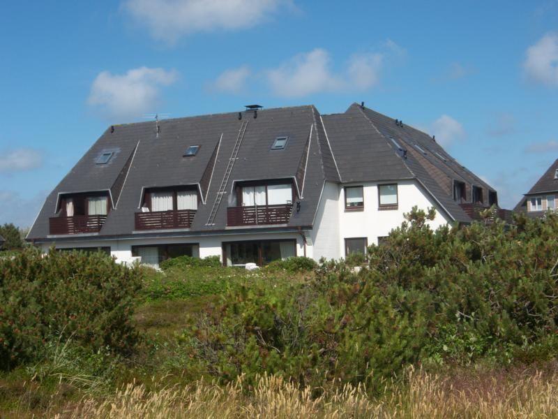 Ein zweistöckiges Haus mit Balkon und Dachfenstern, umgeben von Grünflächen.