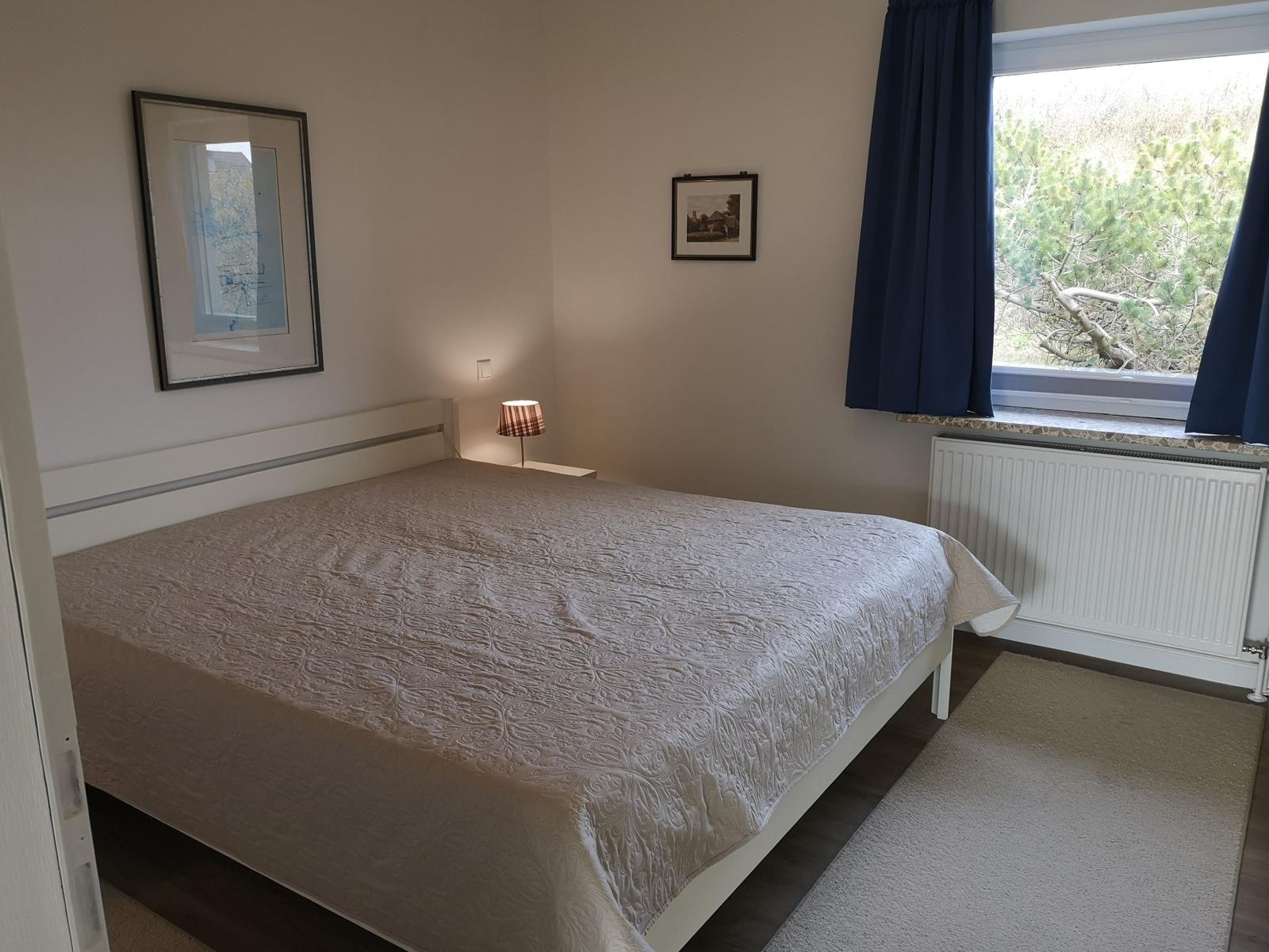 Schlafzimmer mit Bett, Fenster und Wandbildern.