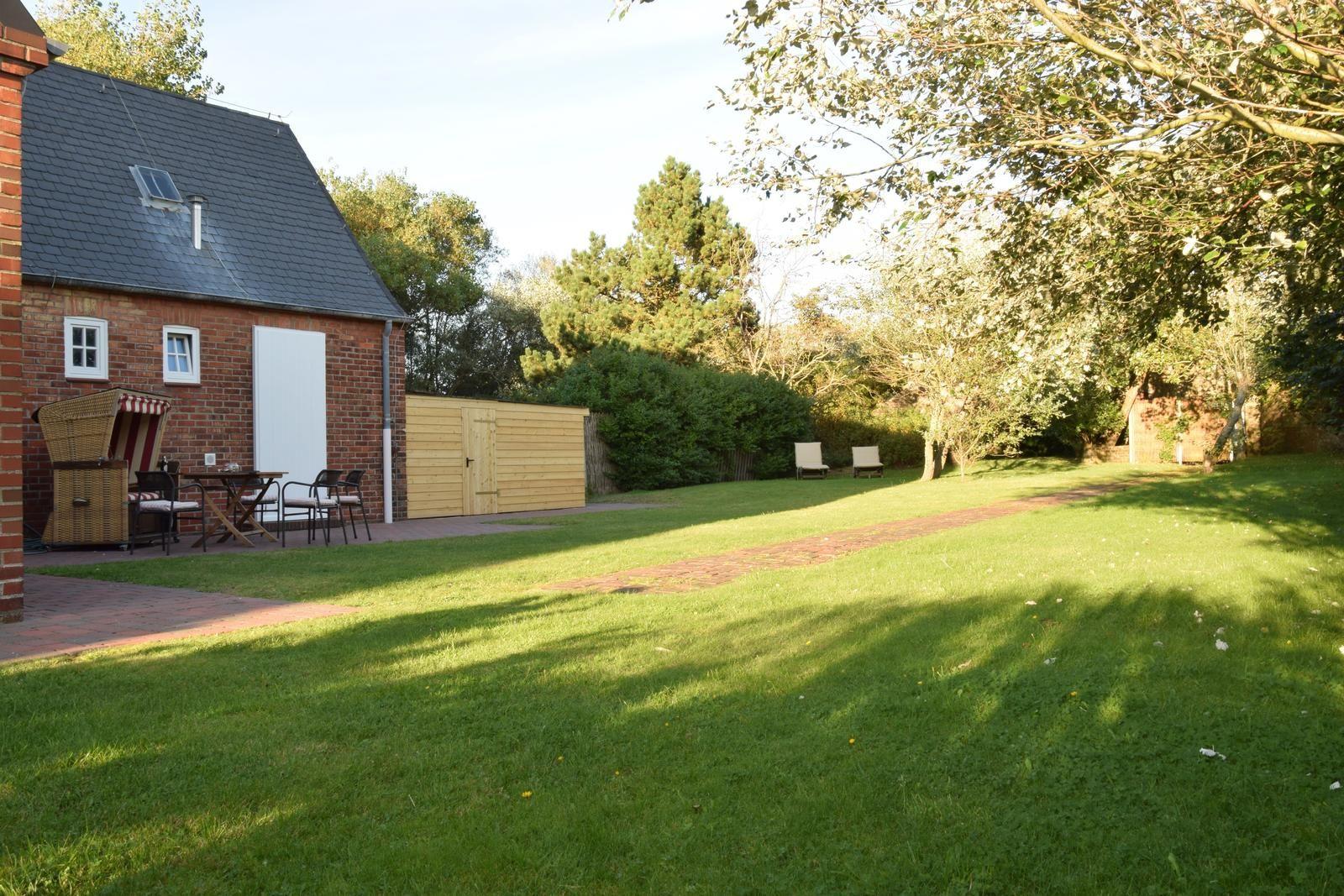 Haus mit Garten, Terrasse und Sitzgelegenheiten unter Bäumen.