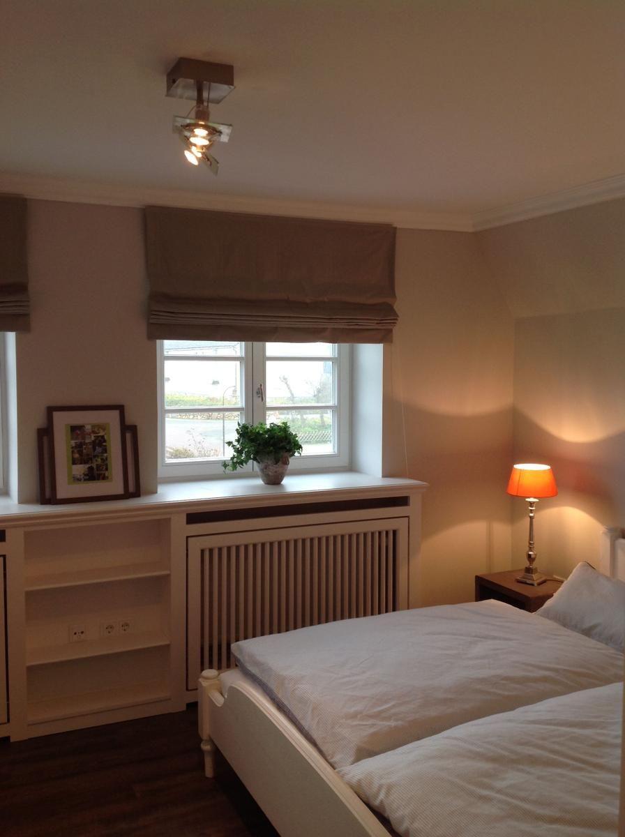 Schlafzimmer mit Bett, Nachttisch, Lampe und Fenster mit Pflanze.