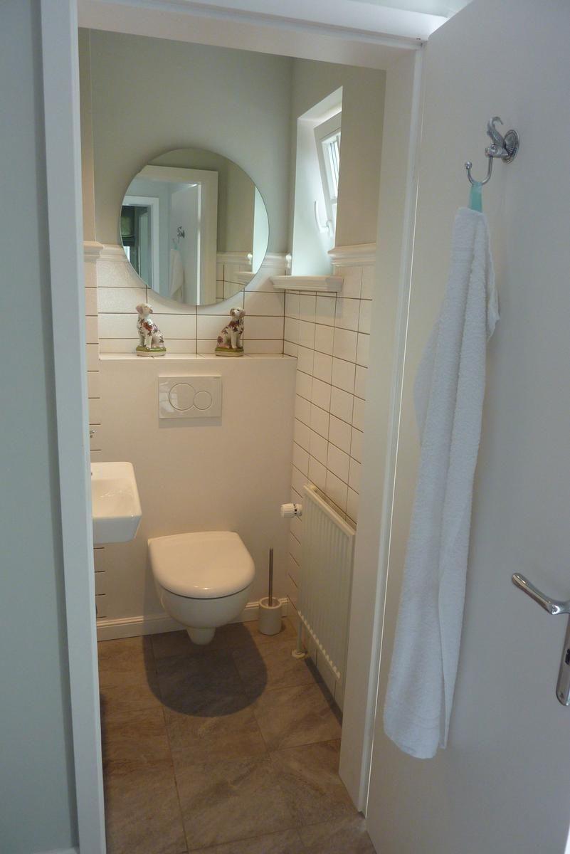 Badezimmer mit Toilette, Waschbecken und runden Spiegel. Handtuch hängt an Tür.