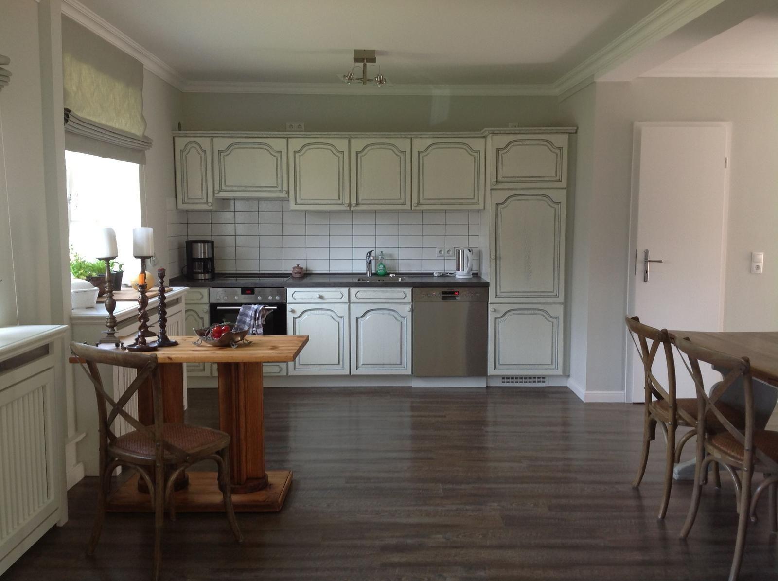 Küche mit weißen Schränken, dunklem Holzboden und Essbereich.