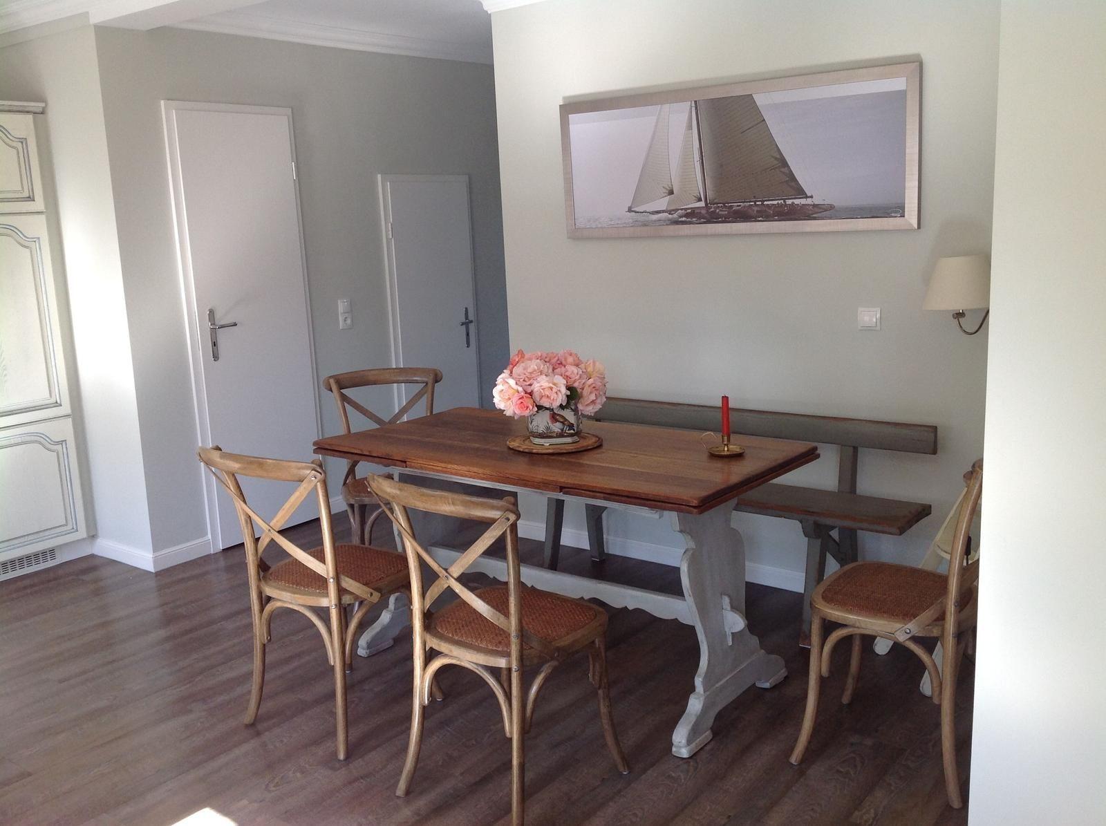 Essbereich mit Holztisch, Stühlen und Bänken. Wandbild zeigt Segelyacht.