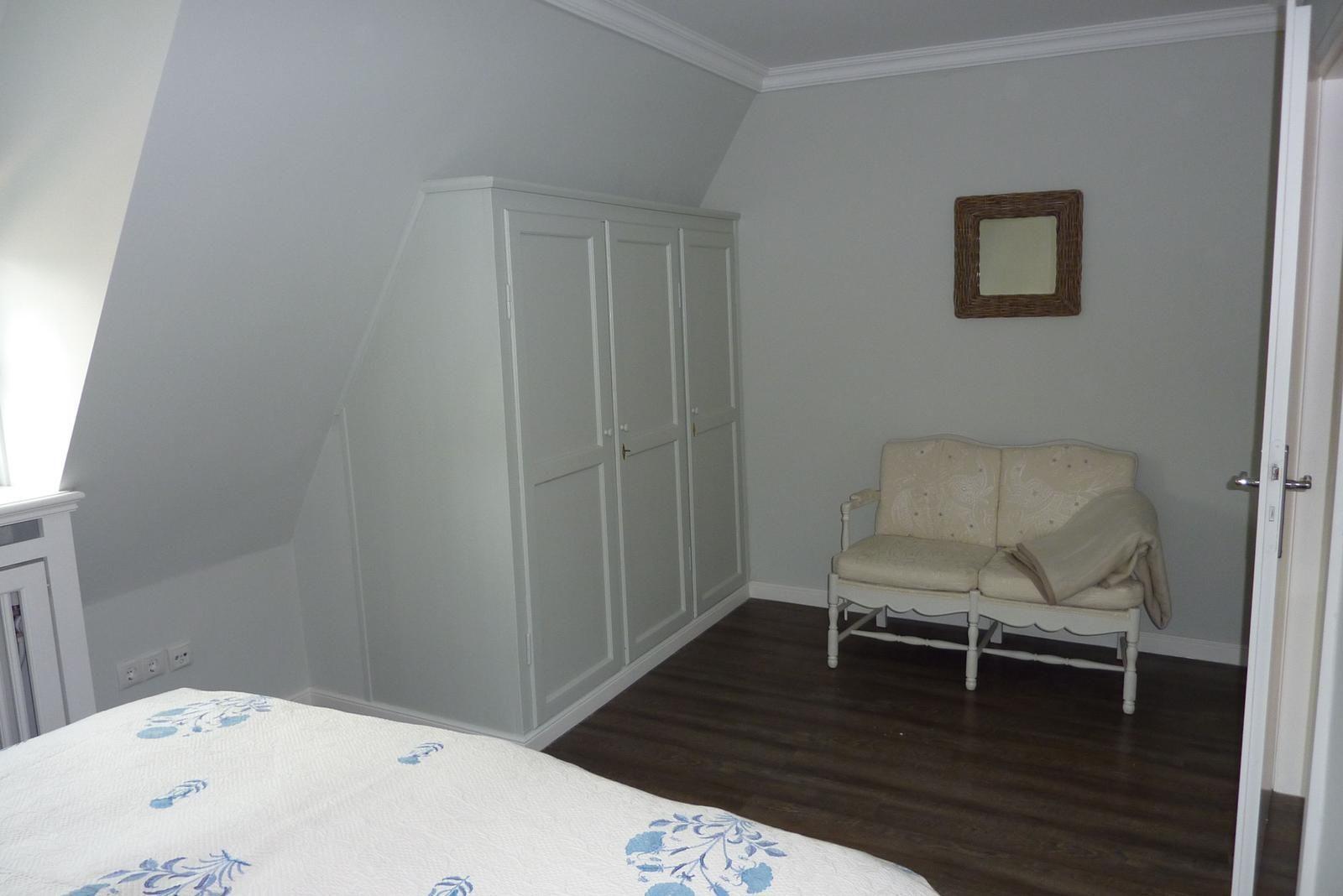 Schlafzimmer mit Dachschräge, Kleiderschrank, Sessel und Holzboden.
