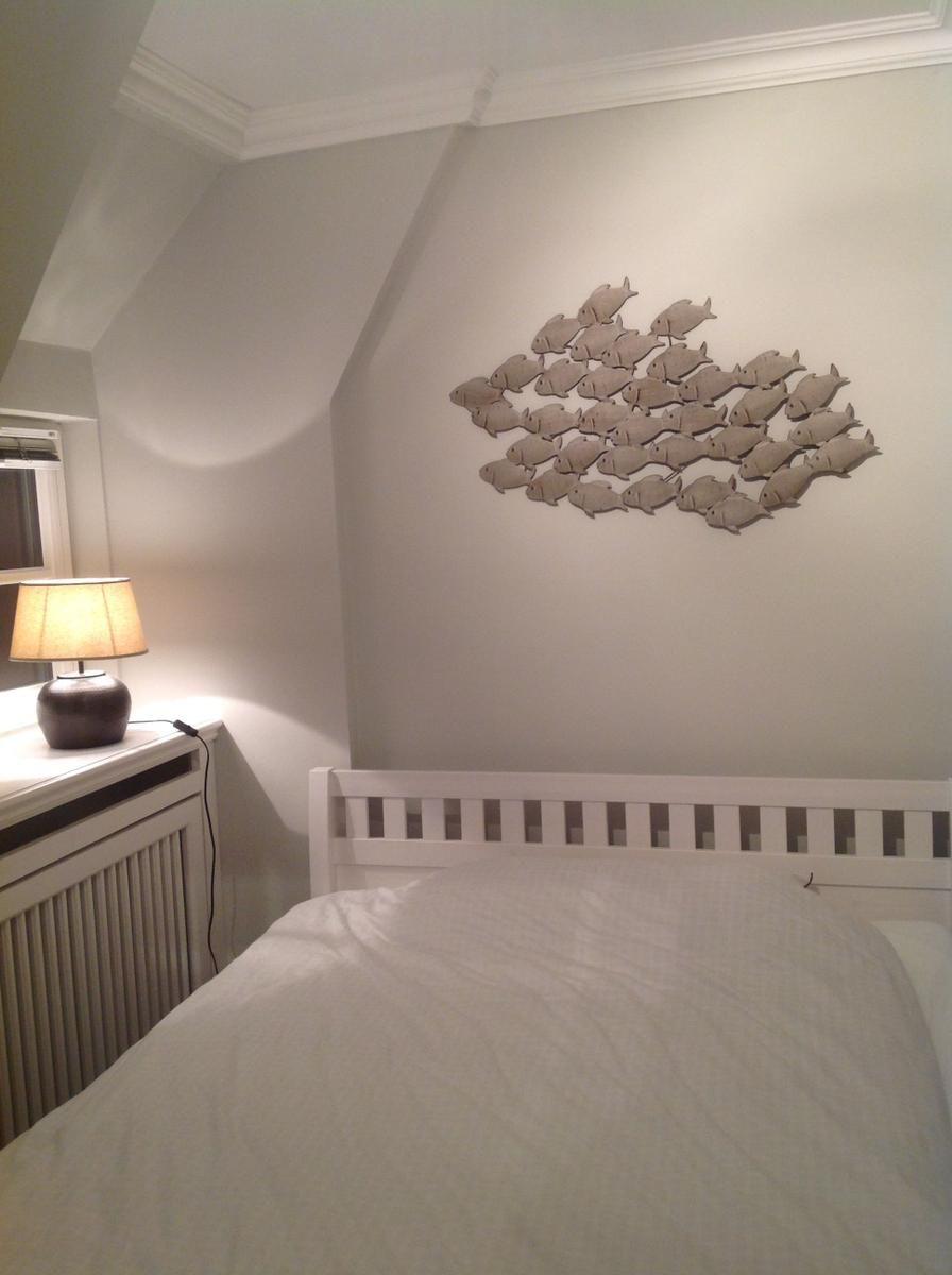 Schlafzimmer mit Bett, Wanddekoration und Nachttisch mit Lampe.