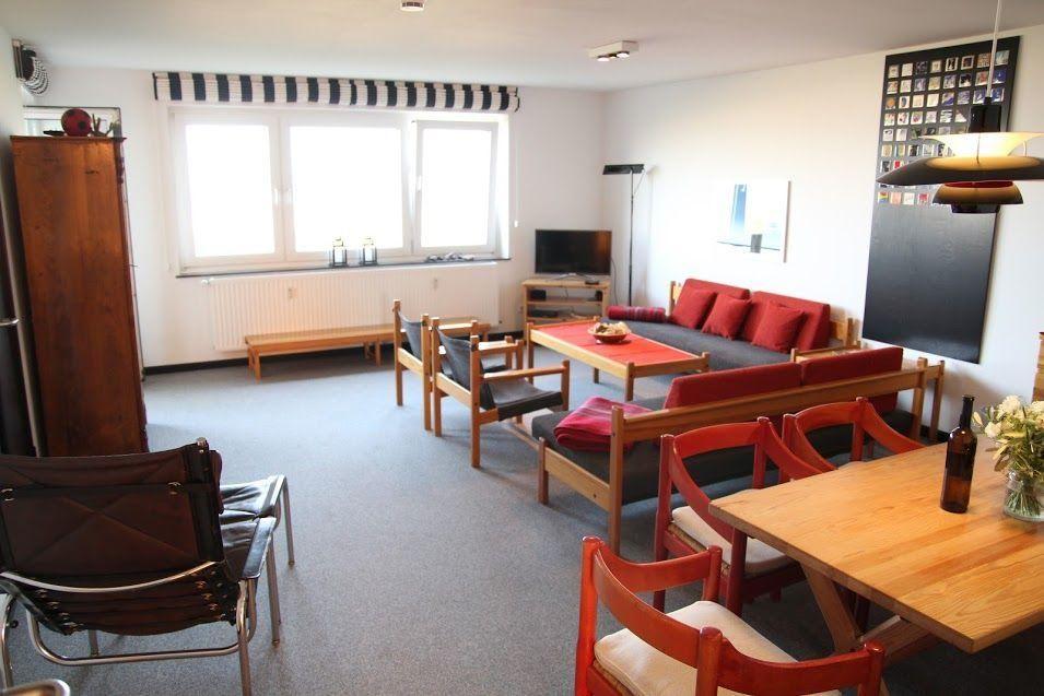 Wohnzimmer mit Sofa, Tisch und Stühlen. Fenster mit Streifenrollo.