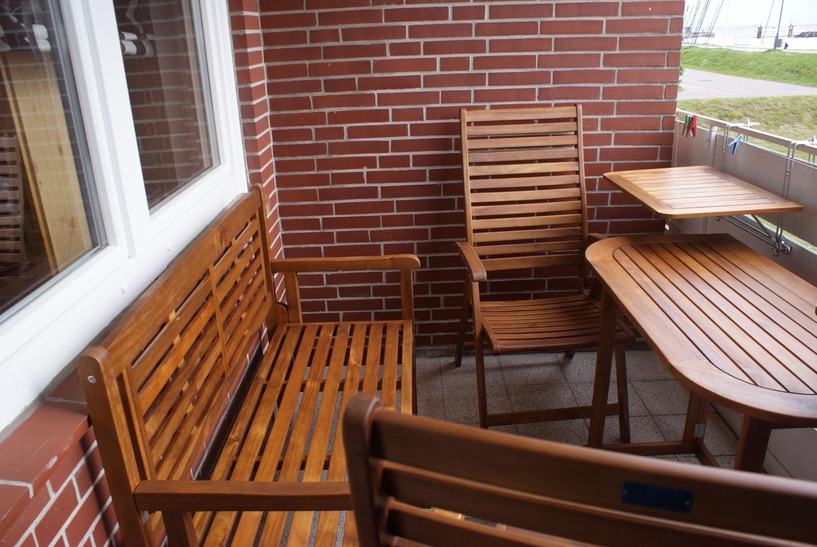 Terrasse mit Holzmöbeln, roter Ziegelwand und Blick auf Grünfläche.