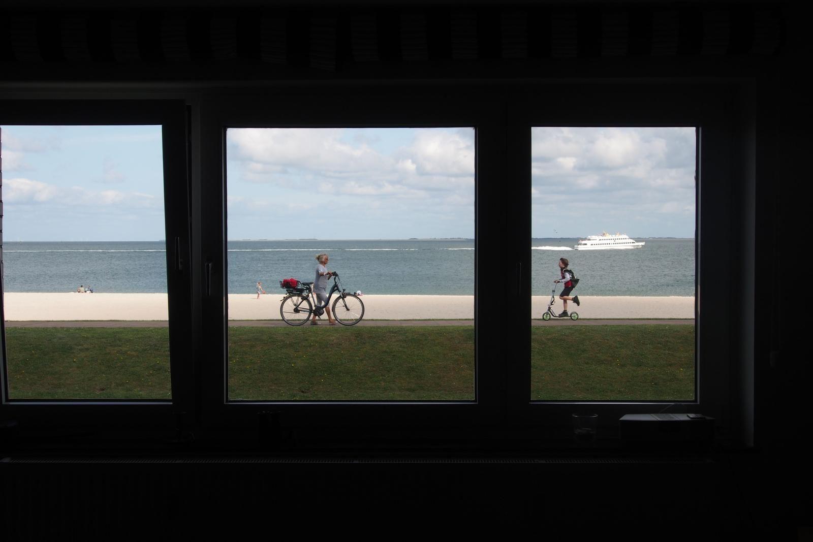 Durch Fenster blickt man auf Strand, Meer und Schiff.