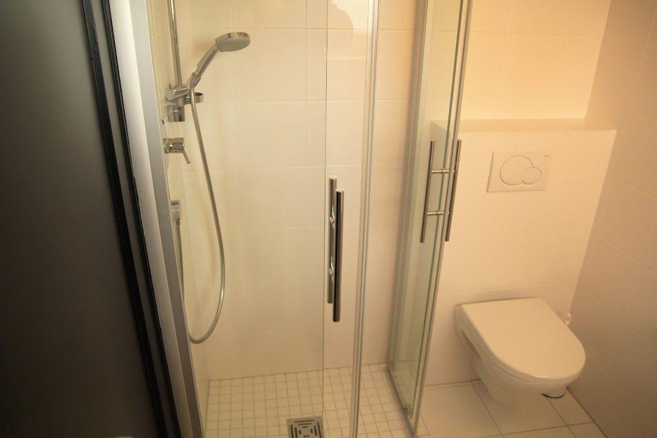 Dusche mit Duschbrause und WC in weißer Fliesenwand