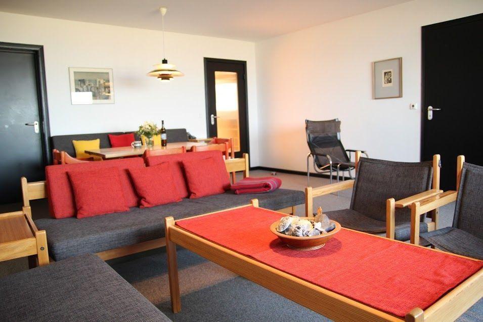 Wohnbereich mit Sofa, Tisch und Stühlen. Rote Kissen und Tischdecke.