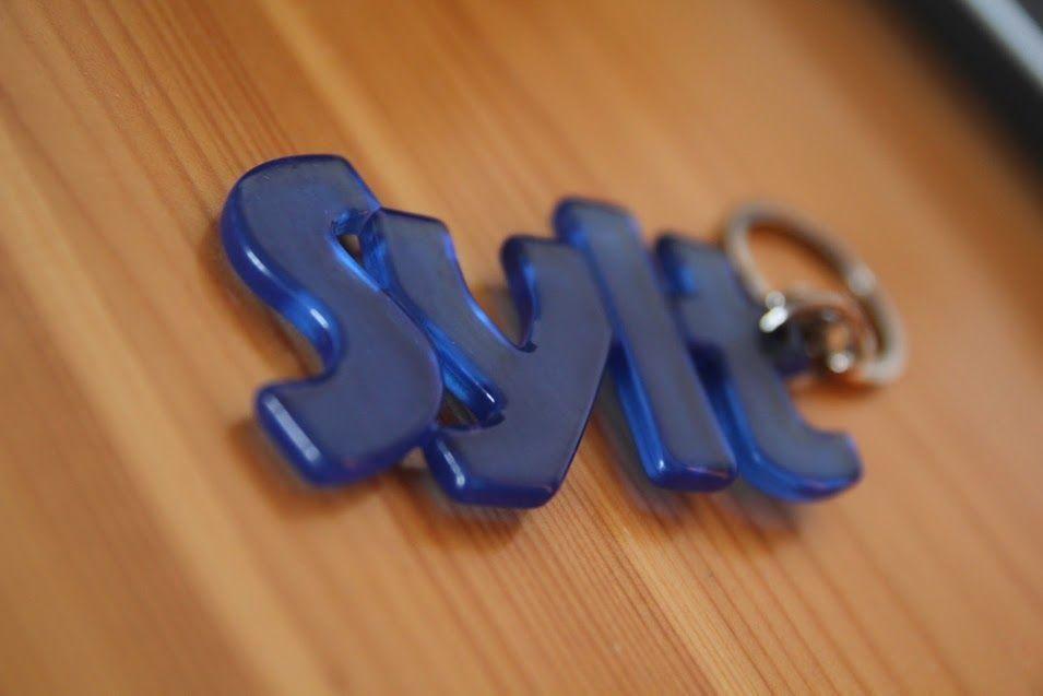 Blauer Schlüsselanhänger mit Buchstaben liegt auf Holzoberfläche.