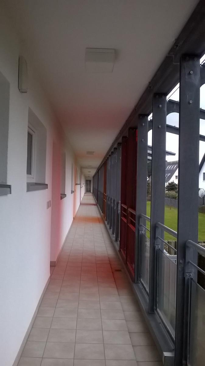 Langgezogener Flur mit Fenstern und Balkon mit Metallgeländer.