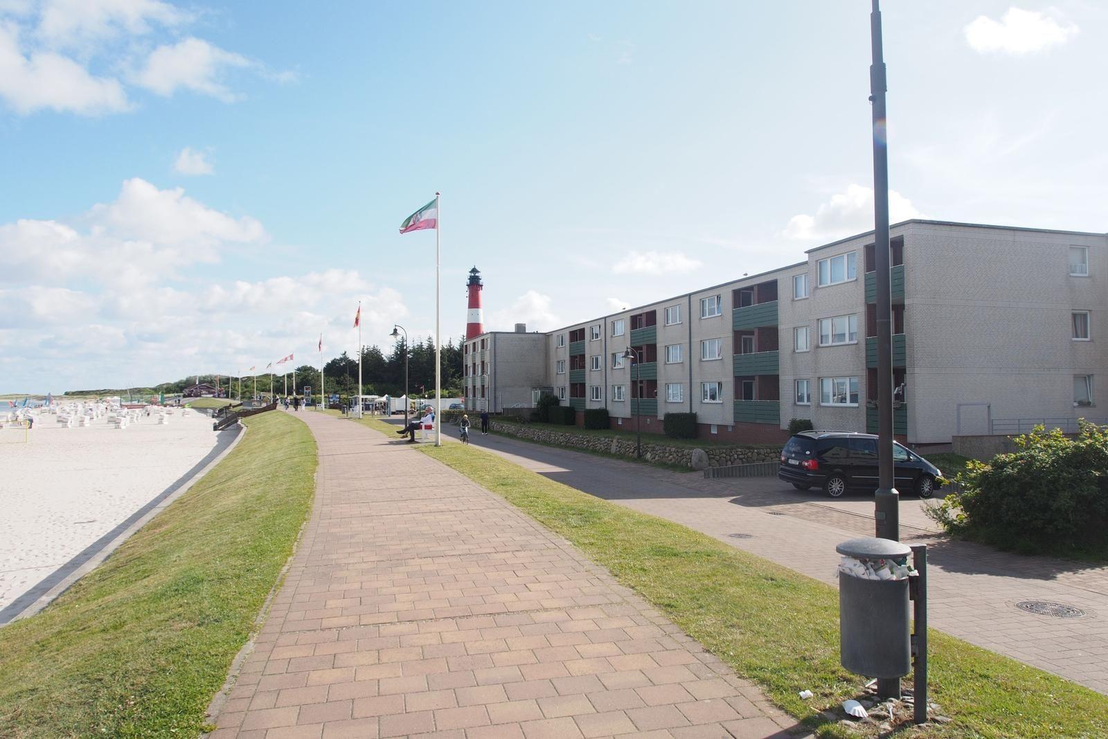Strandpromenade mit Wohnhaus und Leuchtturm im Hintergrund.