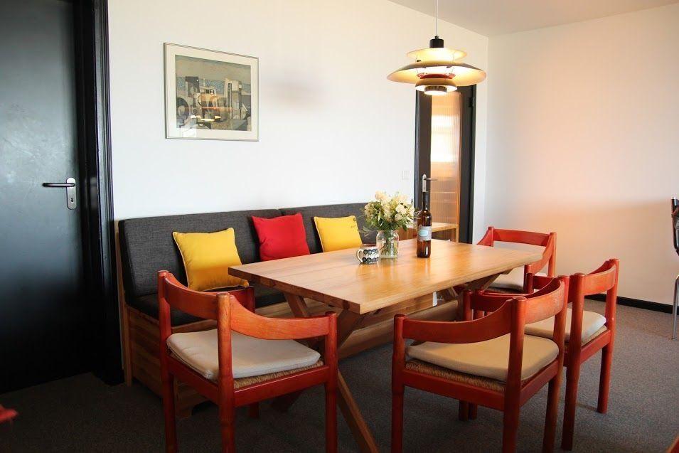 Essbereich mit Holztisch, roten Stühlen und Sofa mit Kissen.