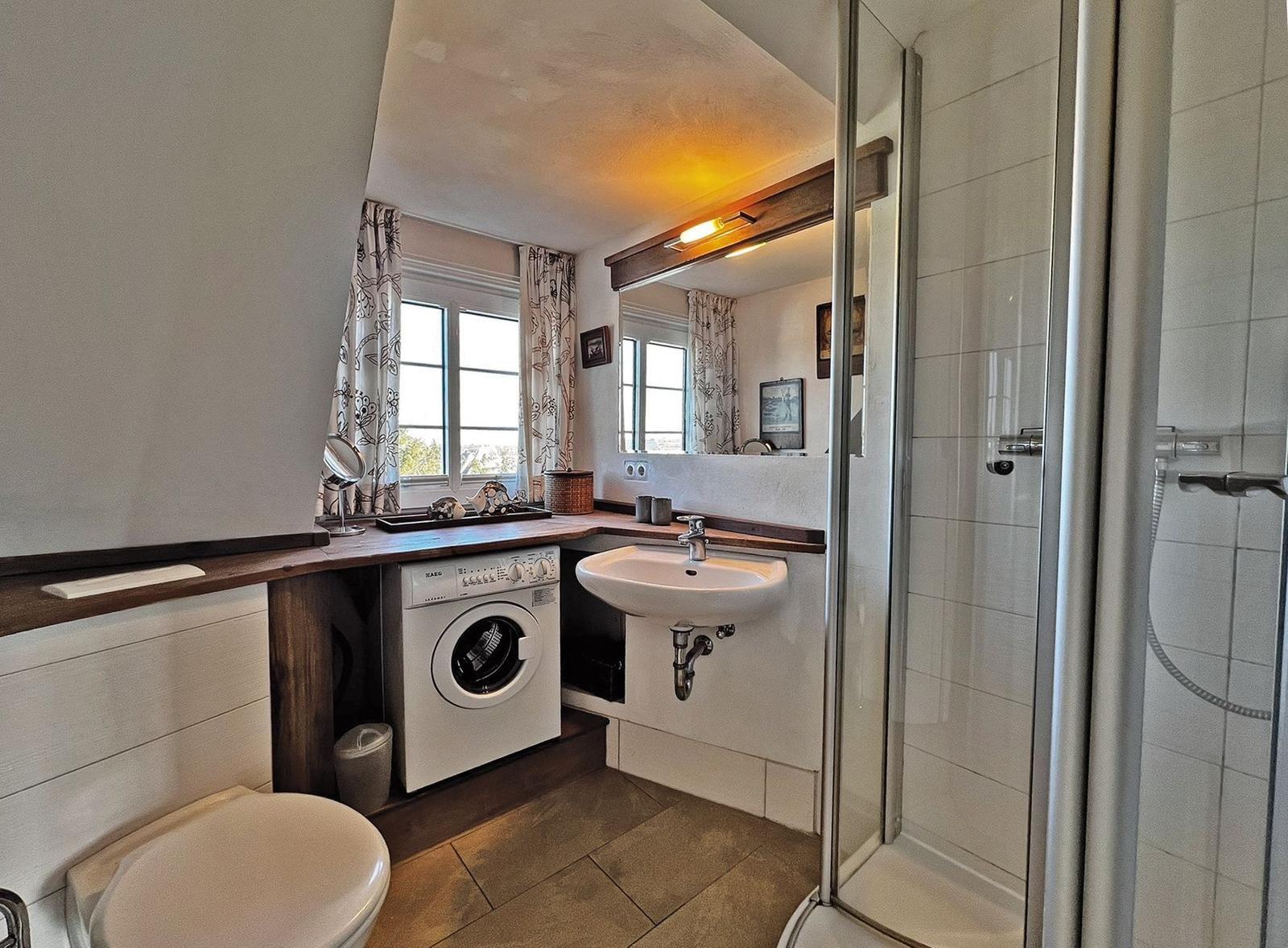 Badezimmer mit Dusche, Waschmaschine und Waschbecken unter Fenster.