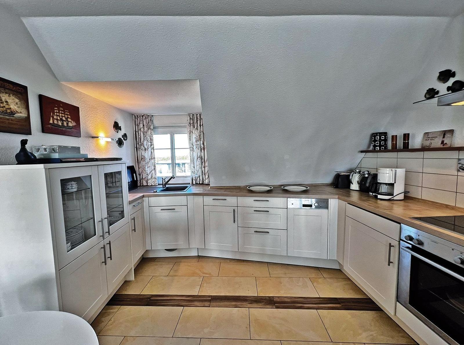 Küche mit weißen Schränken, Holz Arbeitsplatten und Fenster mit Vorhängen.