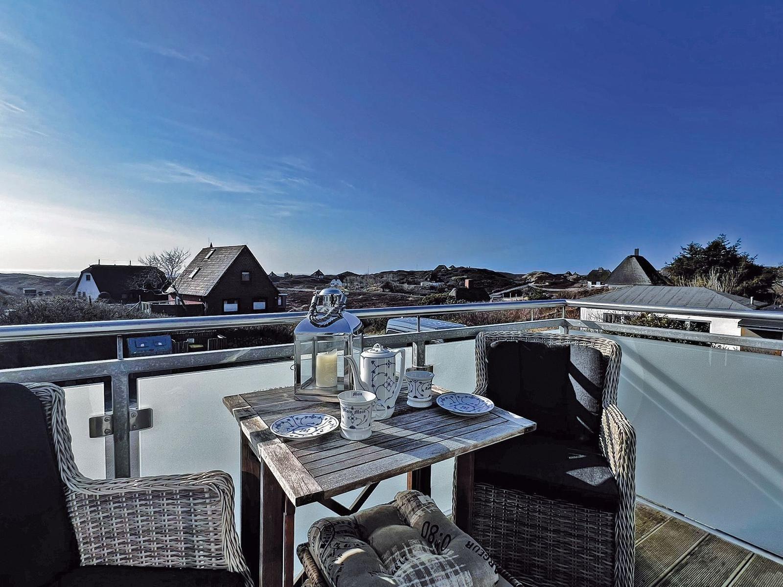 Terrasse mit Tisch, Stühlen und Blick auf Häuser und Hügel.