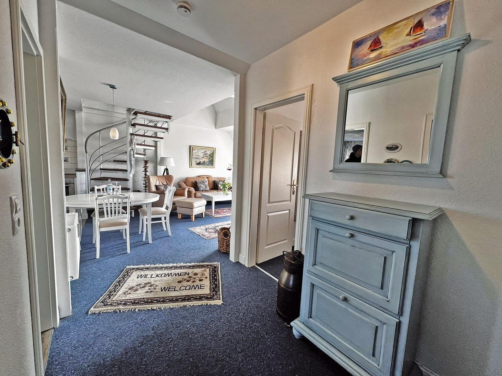 Eingangsbereich mit blauem Teppich und Spiegelschrank. Blick in Wohn- und Essbereich mit Treppe.