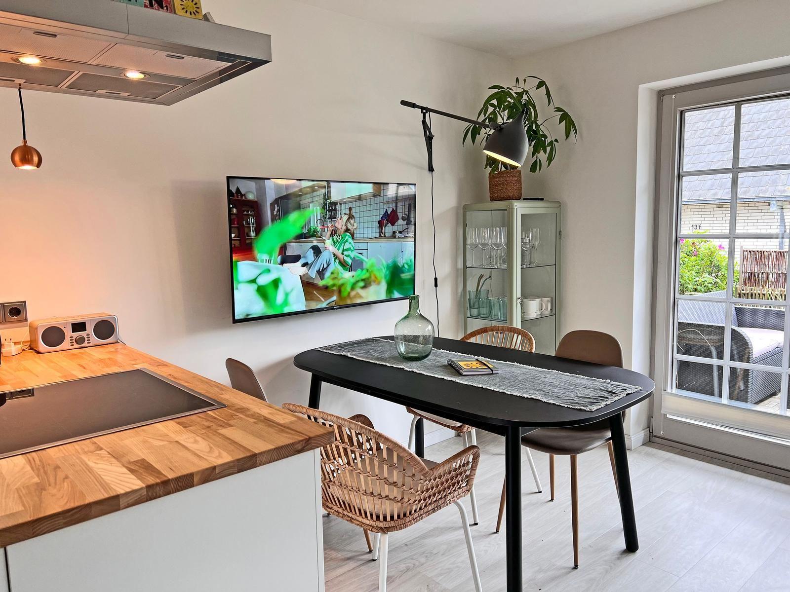 Küche mit Essbereich, Fernseher an der Wand und Terrasse mit Sitzgelegenheit.