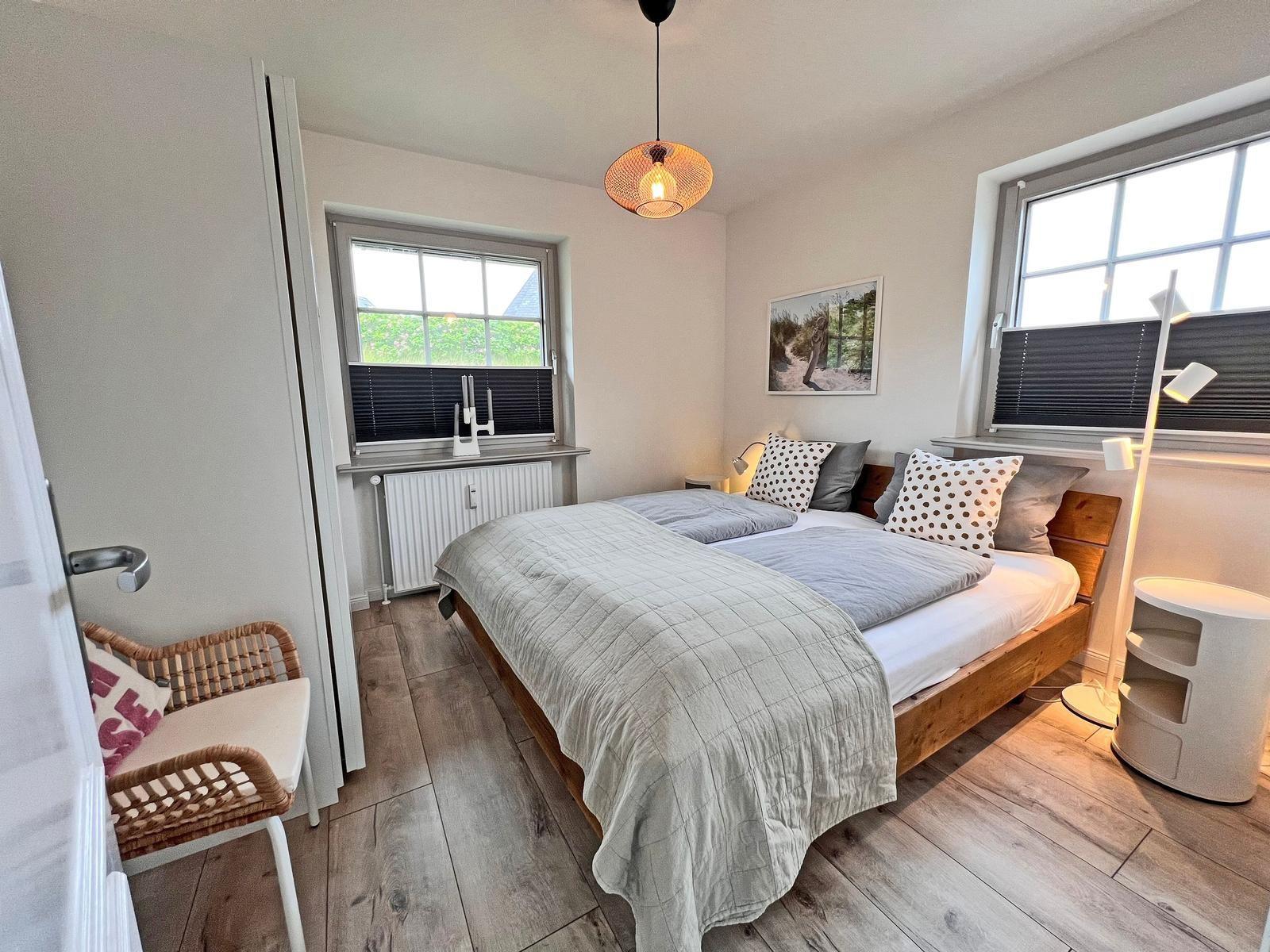 Schlafzimmer mit Doppelbett, Holzboden und zwei Fenstern.