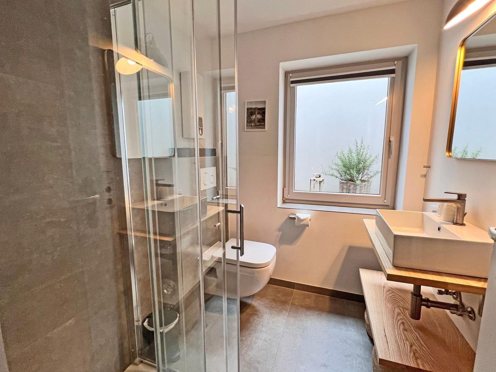 Badezimmer mit Dusche, Toilette und Waschbecken mit Fenster