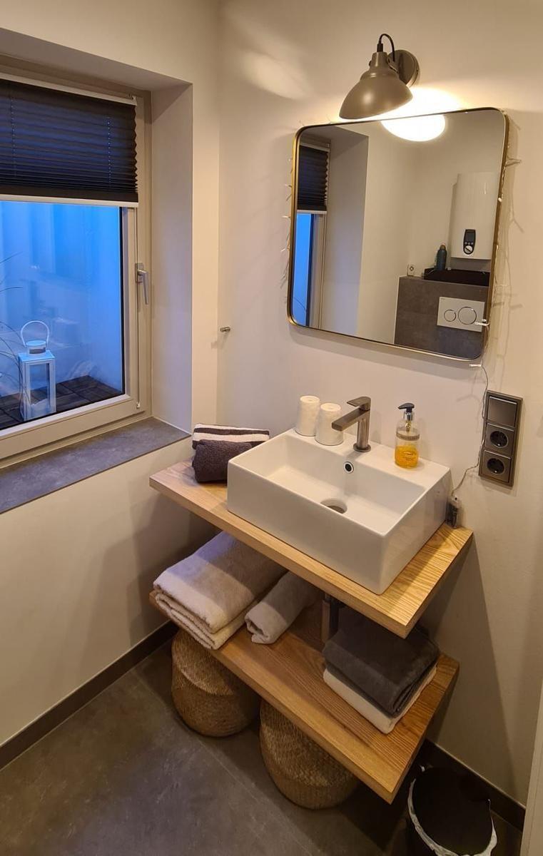 Badezimmer mit Waschbecken, Spiegel und Fenster mit Jalousie.