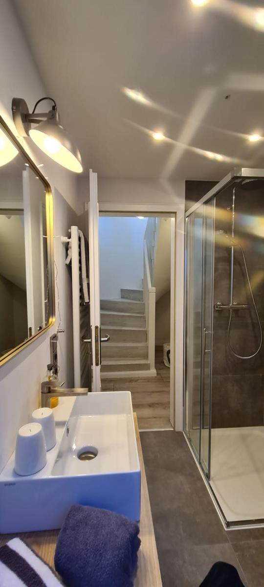 Badezimmer mit Dusche, Waschbecken und Spiegel. Treppe führt nach oben.