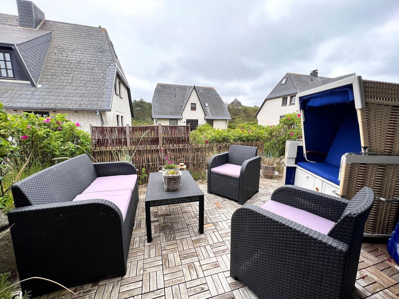 Terrasse mit Sitzgruppe, Liegestuhl und Gartenzaun.