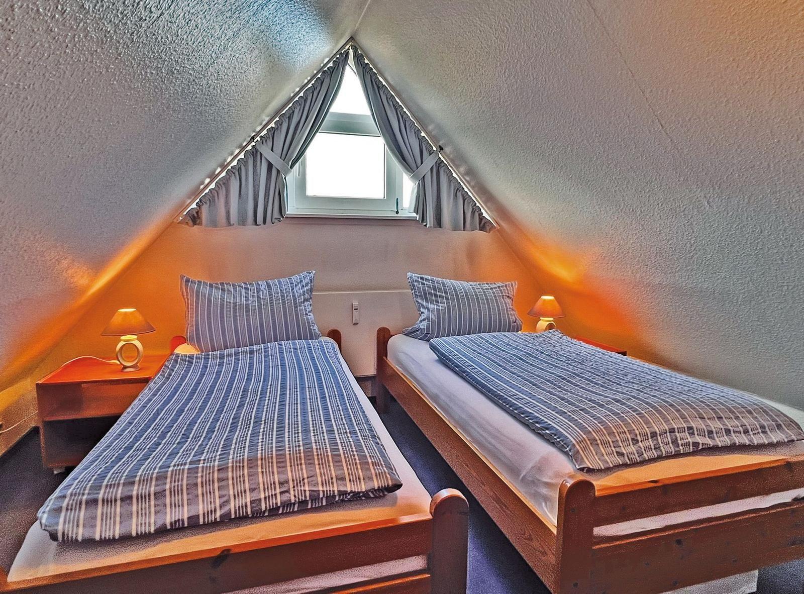 Zwei Einzelbetten unter Dachschrägen mit Nachttischen und Lampe.