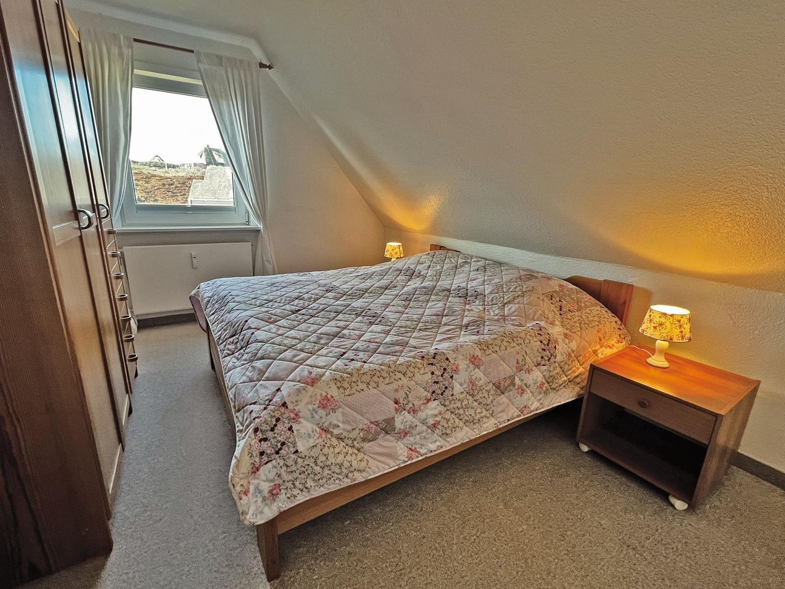 Schlafzimmer mit Dachschrägen, Bett, Nachttisch und Fenster.