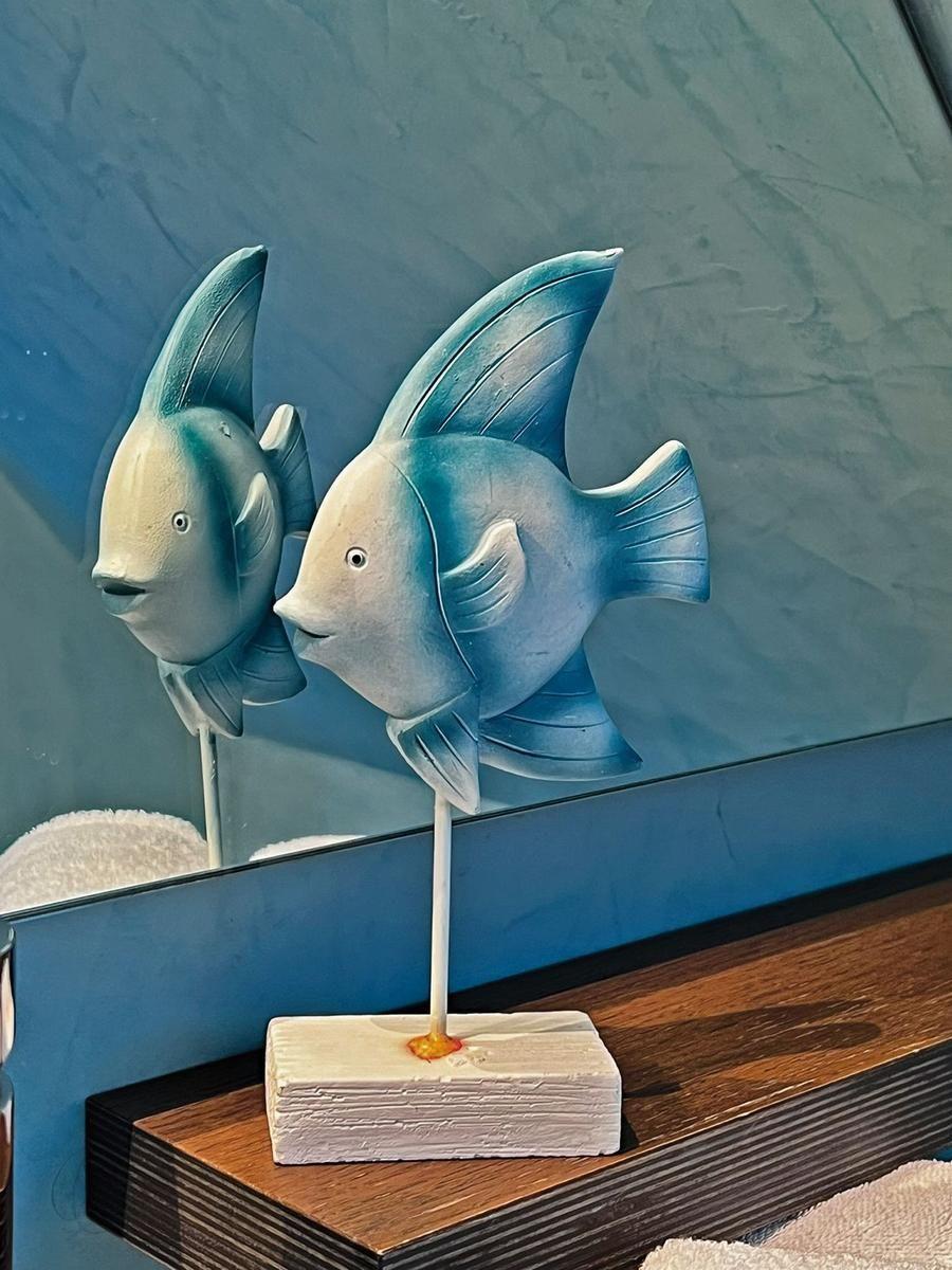Zwei Fischfiguren auf Holzsockel vor blauer Wand