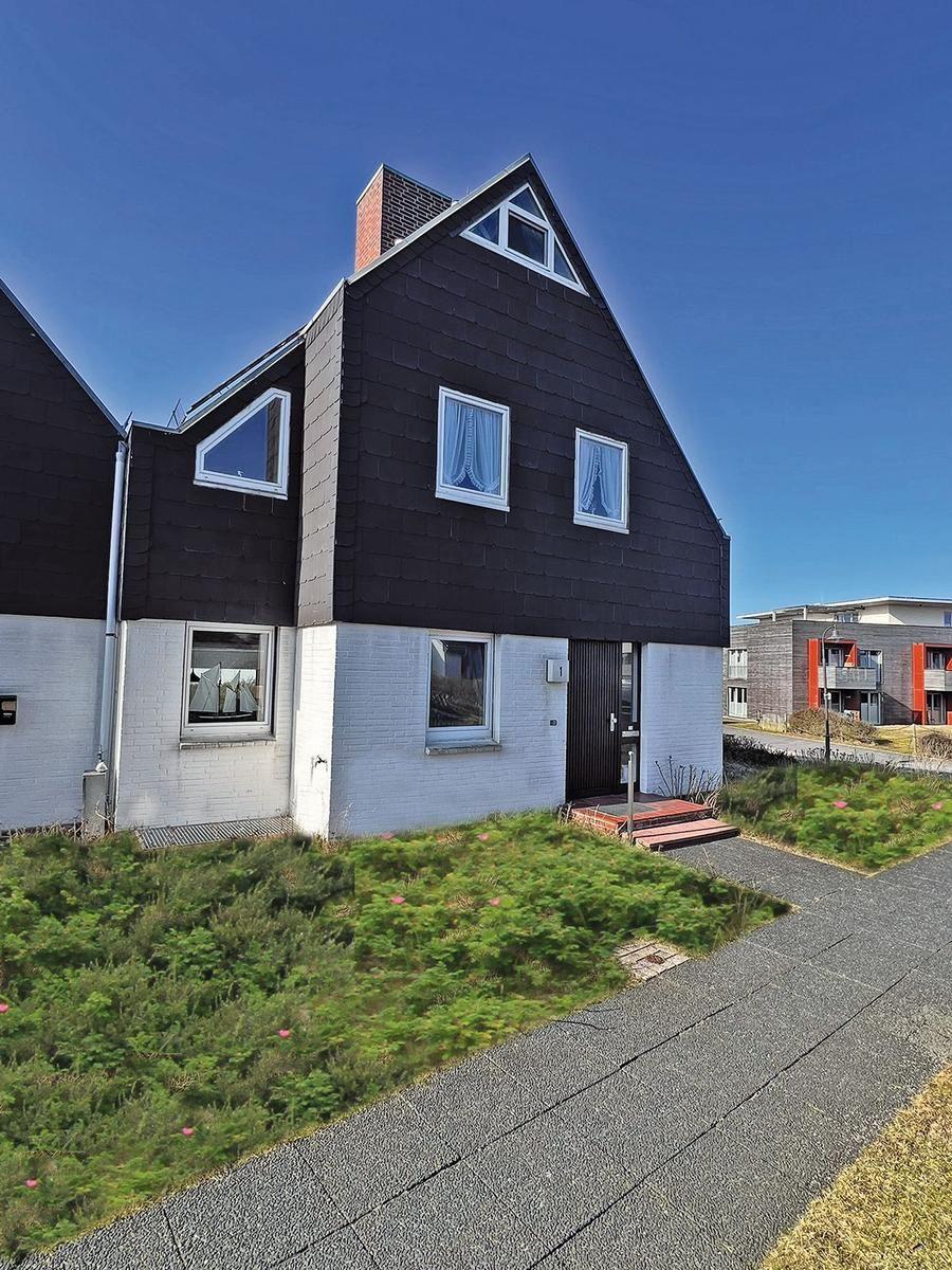 Haus mit schwarzem Dach und weißer Fassade, Eingangstür und Fenster mit Vorhängen.