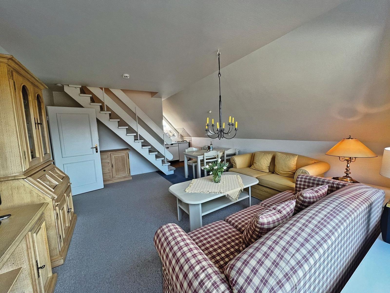 Wohnbereich mit Sofa, Tisch und Stufen zur Küche.