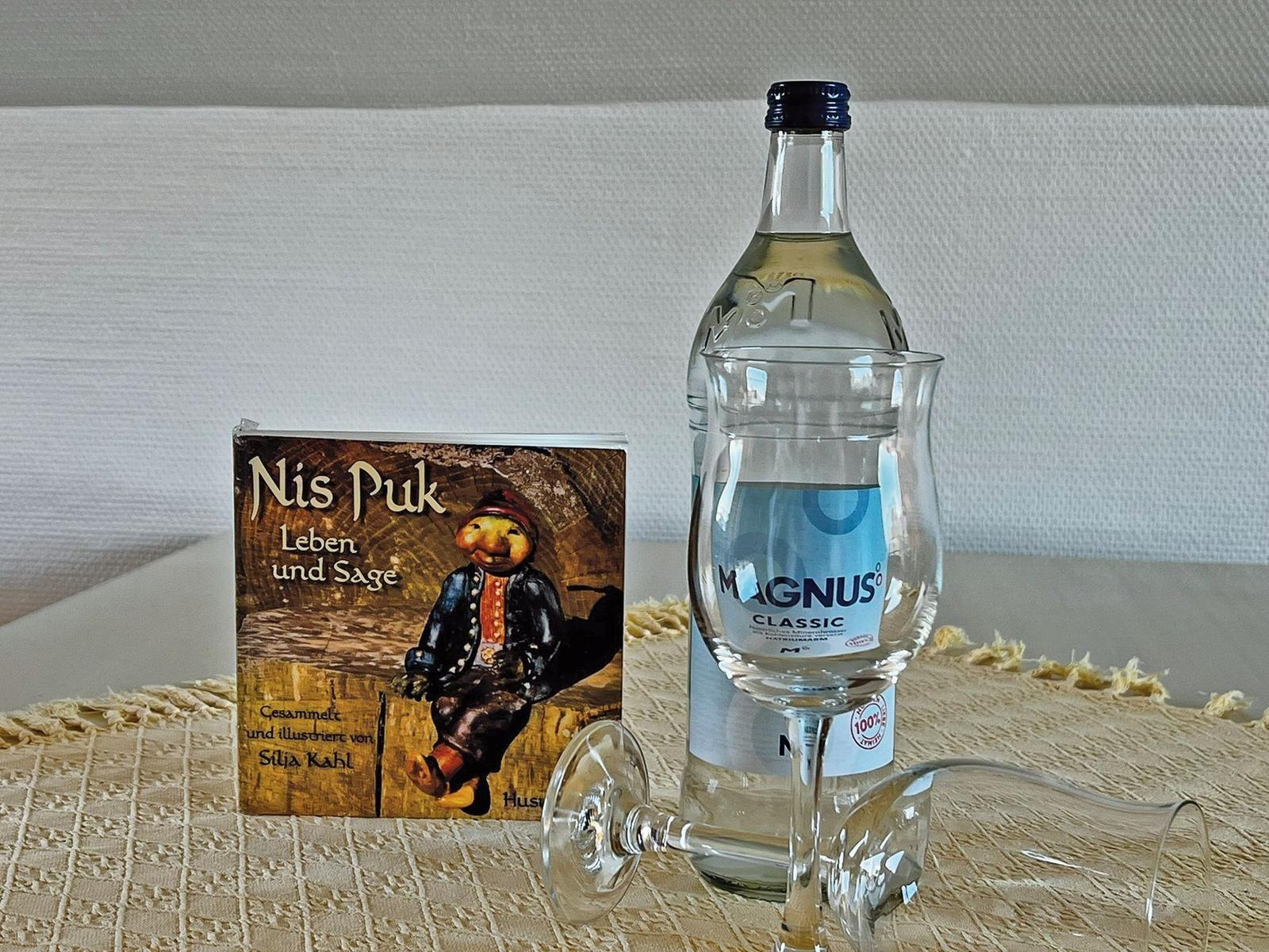 Ein Buch und eine Flasche mit zwei Gläsern auf einem Tisch.