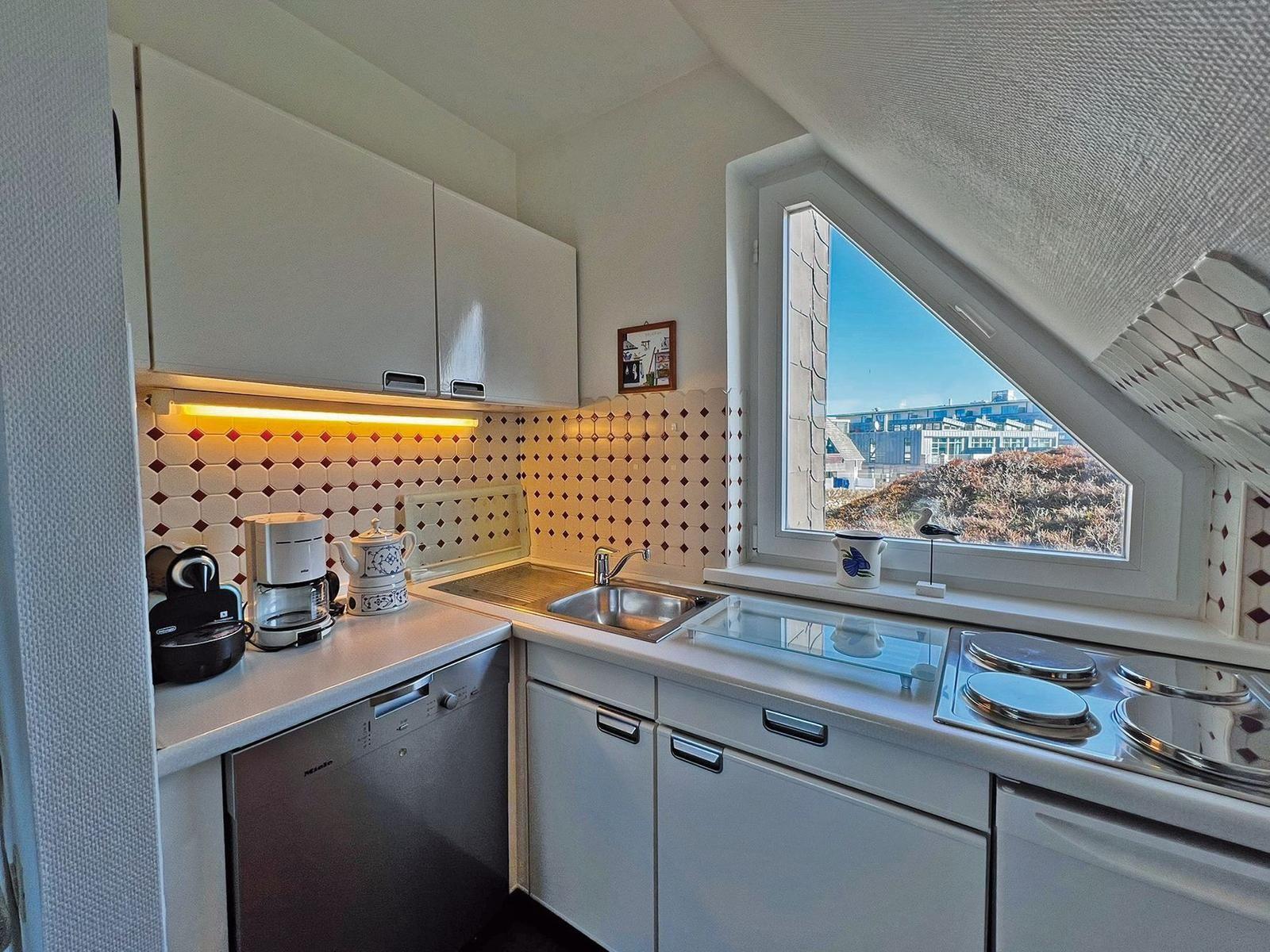 Küche mit Spüle, Herd und Waschmaschine unter Dachschrägen mit Blick auf Außenbereich.