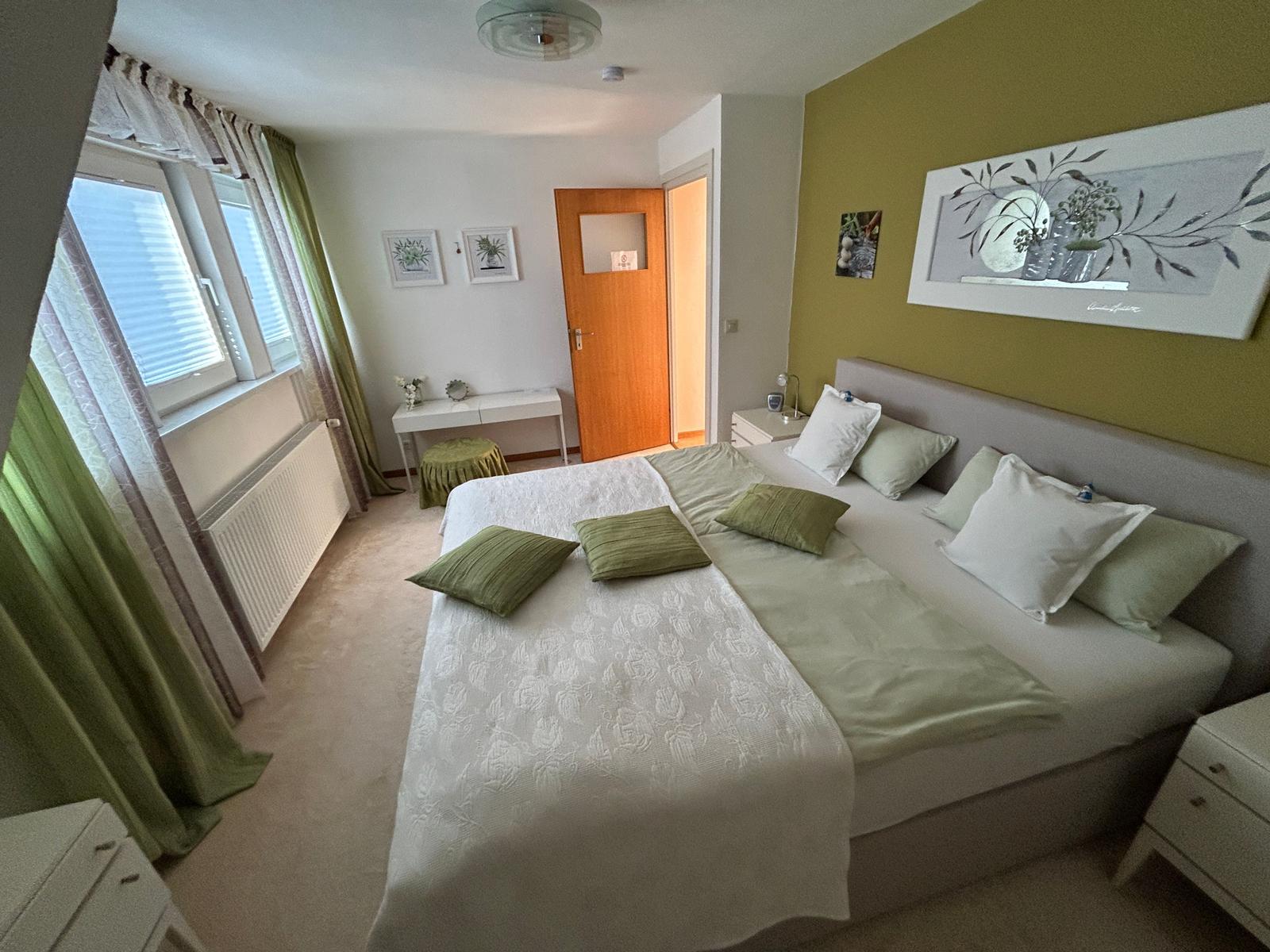 Schlafzimmer mit Doppelbett, grünen Kissen und Fenster mit Vorhängen.