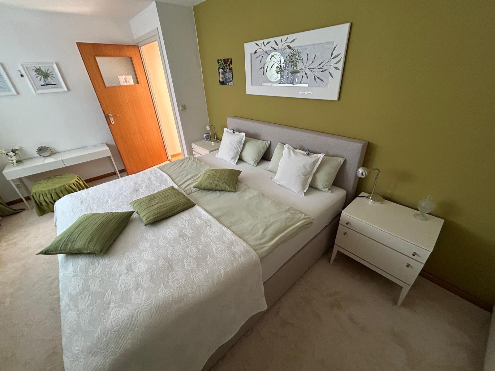 Schlafzimmer mit Bett, Nachttischen und grüner Wand.