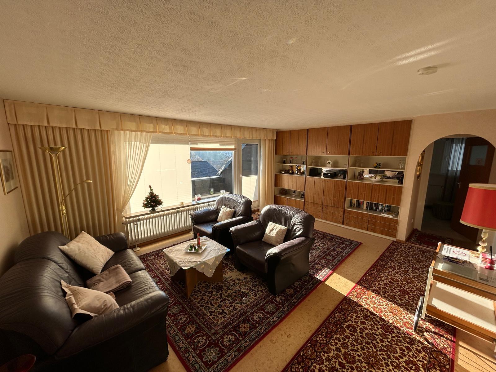 Wohnzimmer mit Ledersofa, zwei Sesseln, Teppich und Holzmöbel.