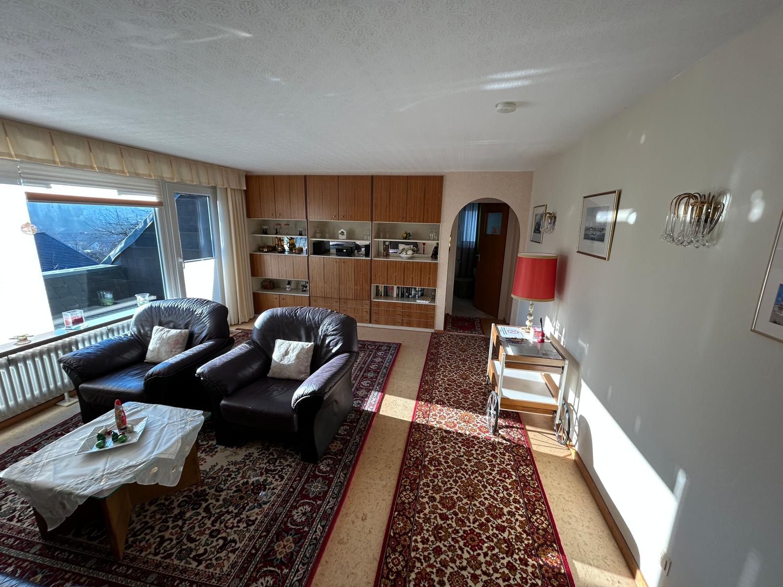 Wohnzimmer mit zwei Sesseln, Teppich und Bücherregal.