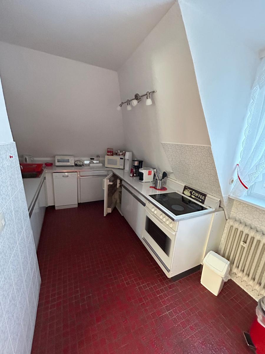 Küche mit rotem Boden, weißen Geräten und Fenster mit Vorhang.