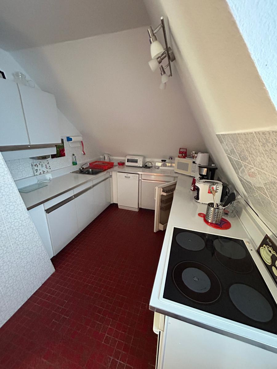 Küche mit rotem Boden und weißen Schränken unter schrägem Dach