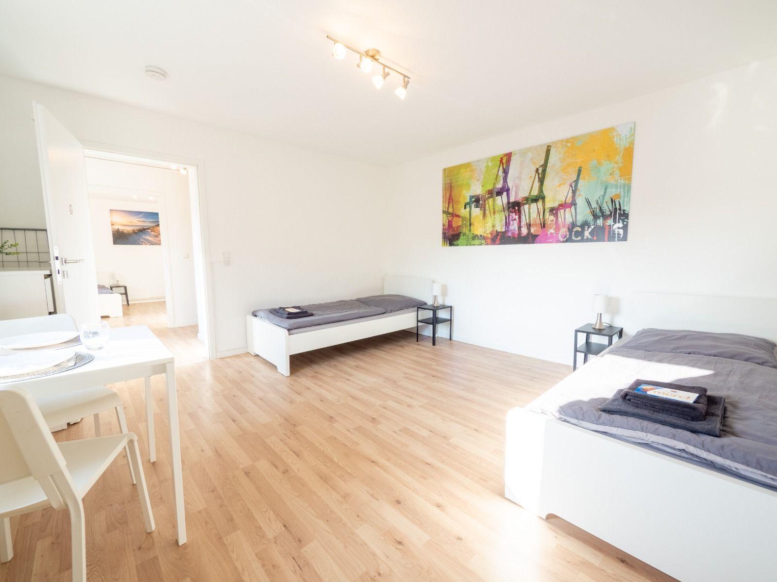 Zimmer mit zwei Betten, Holzboden und Wandbild mit Kränen.