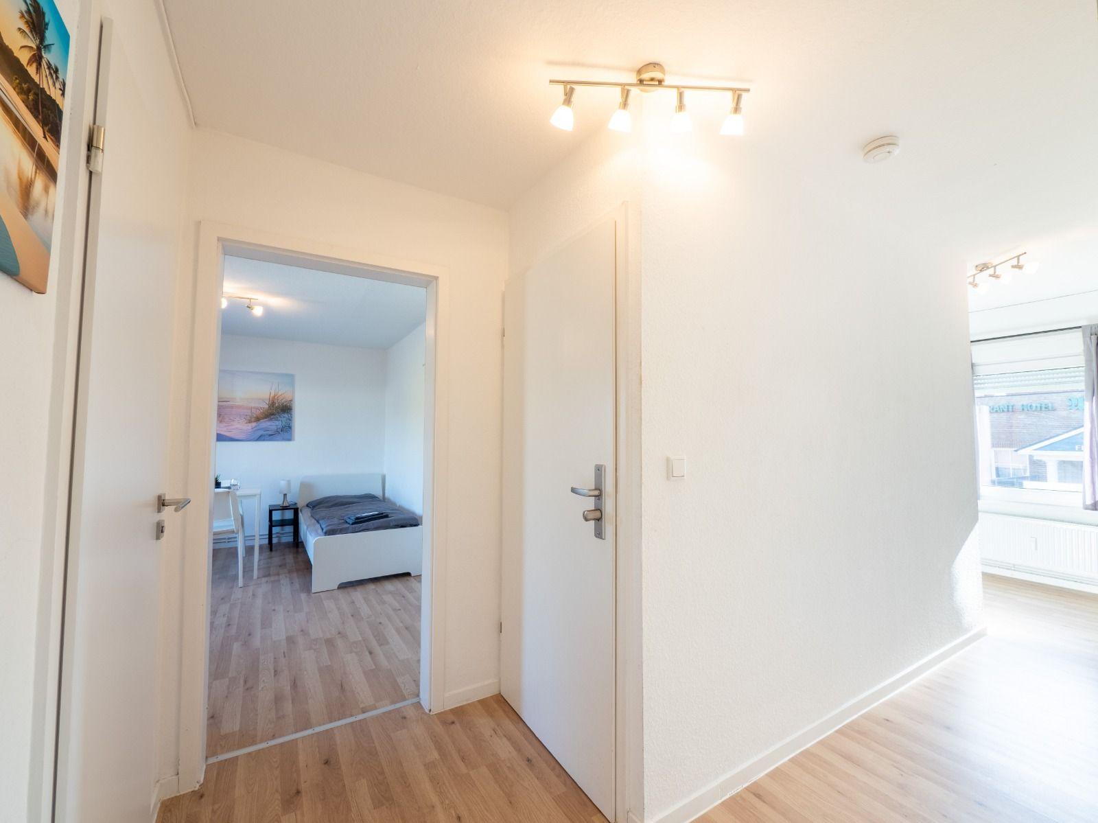 Flur mit Tür zu Schlafzimmer und Fenster. Holzboden und weiße Wände.