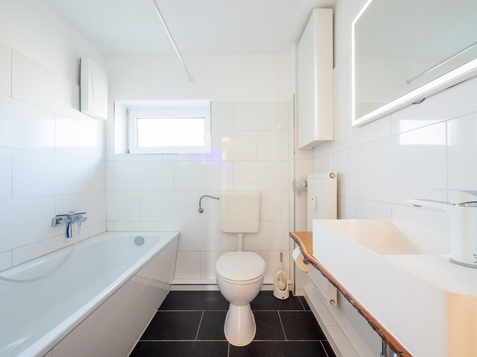 Badezimmer mit Badewanne, Toilette und Waschbecken mit Spiegel.