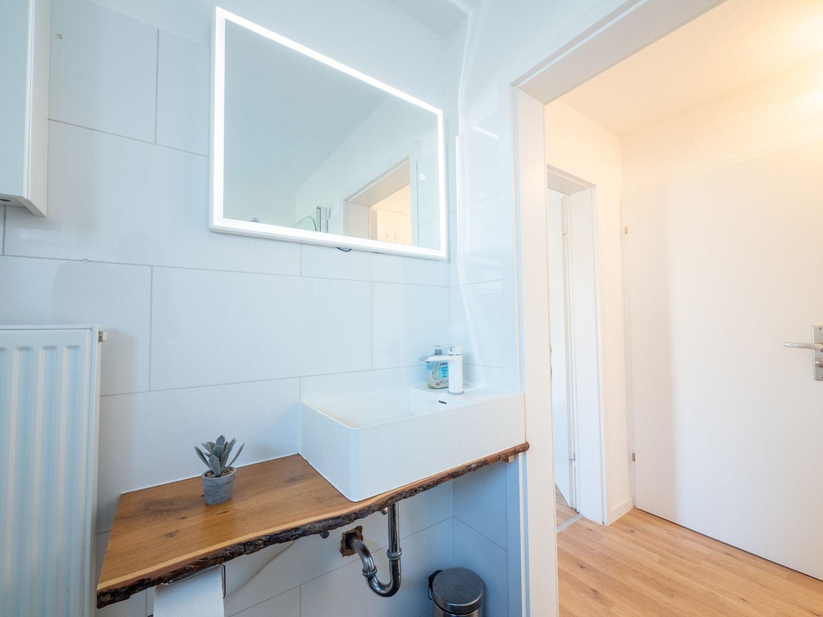 Badezimmer mit Waschbecken, Spiegel und Holzregal.