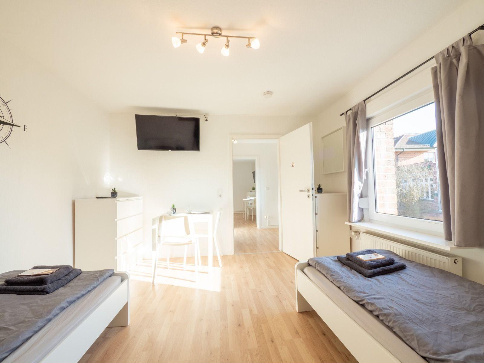 Zwei Betten, TV, Tisch und Fenster mit Blick nach draußen.