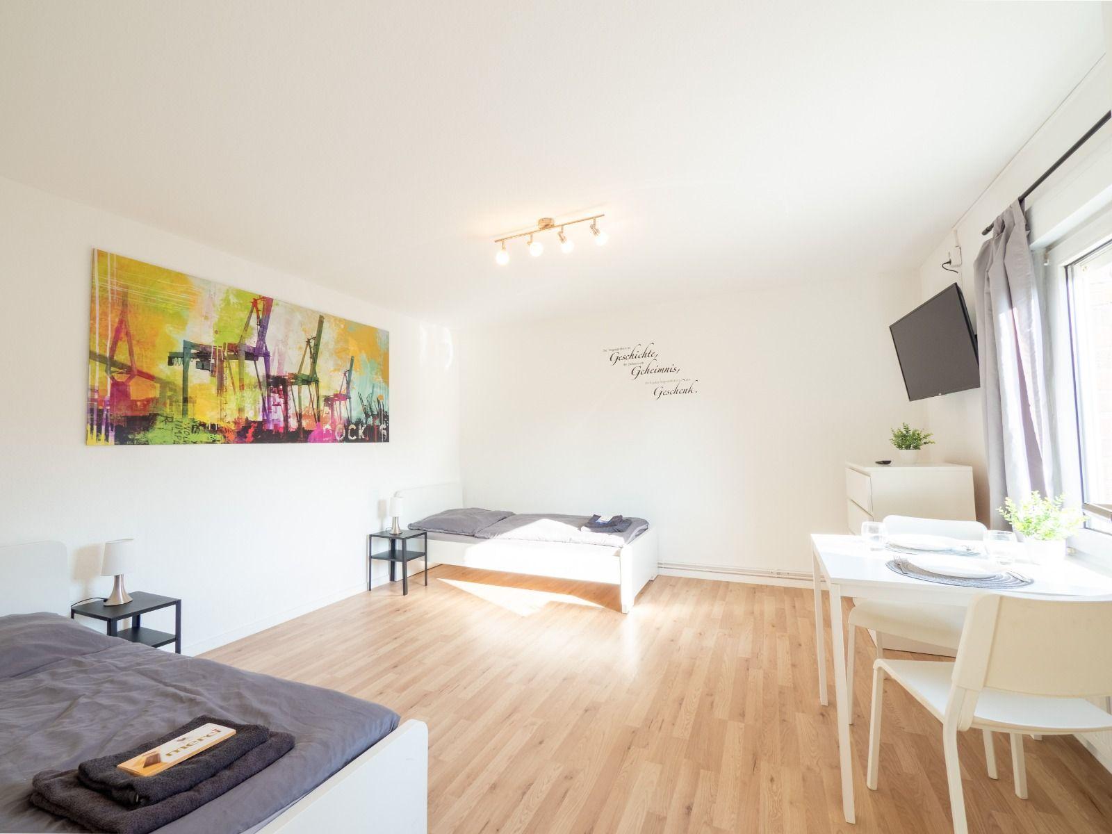 Zimmer mit Bett, Esstisch und Wandbild. Holzboden und Fenster.